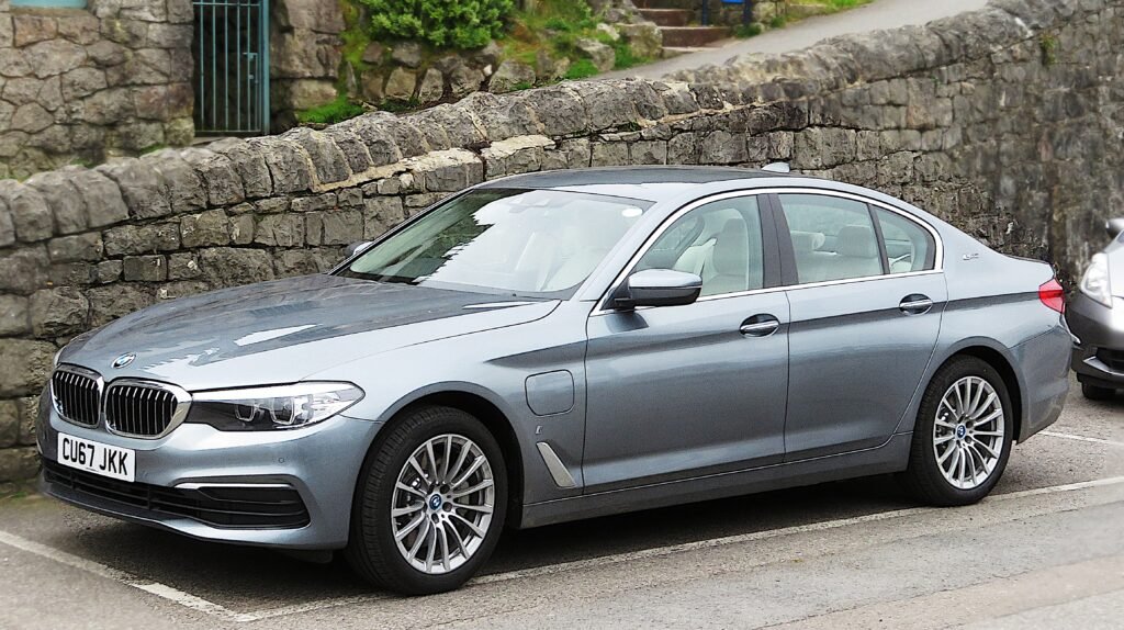 Grey BMW 530e iPerformance plug-in hybrid sedan, front three-quarter view, parked outdoors beside a stone wall.