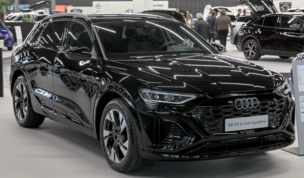 Black Audi Q8 e-tron 55 quattro displayed indoors at an auto show, viewed from the front three-quarter angle.