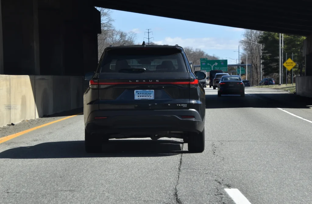 Rear view of a 2026 Lexus TX 350 AWD driving beneath an overpass