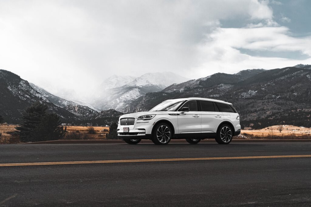 White Lincoln Aviator parked on a two-lane mountain road, front three-quarter view, with snow-dusted peaks under an overcast sky.