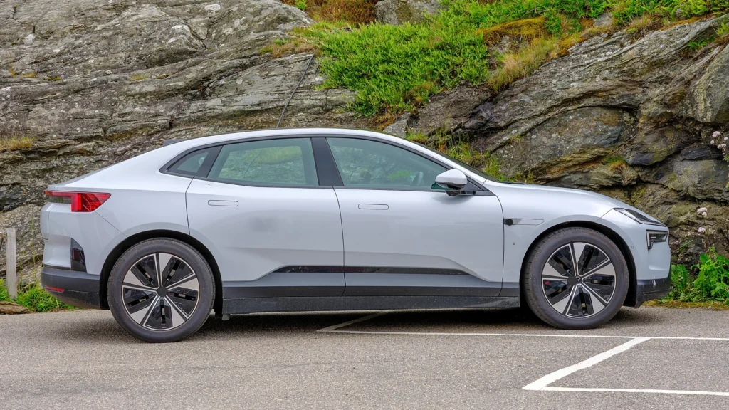 Side profile of a silver Polestar 4 parked beside a rocky landscape.