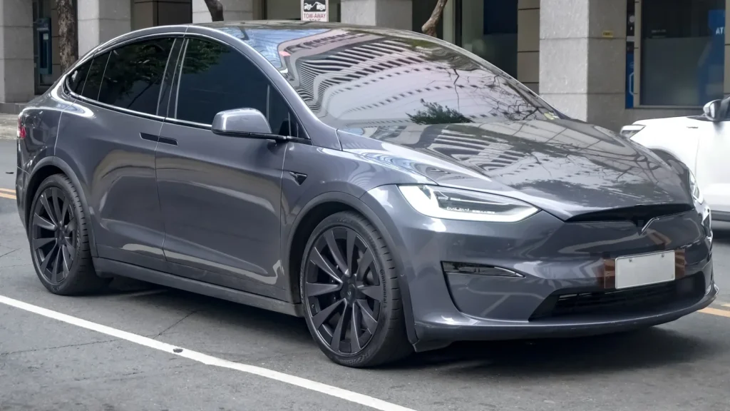 Grey Tesla Model X Plaid parked on a city street, viewed from the front three-quarter angle.