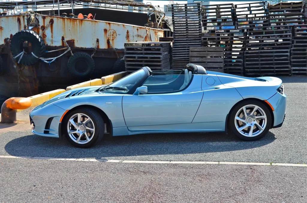 Light-blue first-generation Tesla Roadster parked in Kobe, shown in side profile.